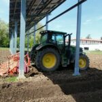 Copilot said: Un tractor en un campo pasando bajo un panel agrivoltaico