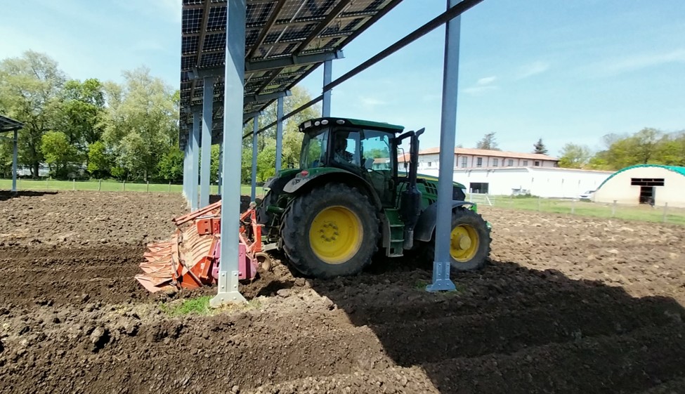 Copilot said: Un tractor en un campo pasando bajo un panel agrivoltaico